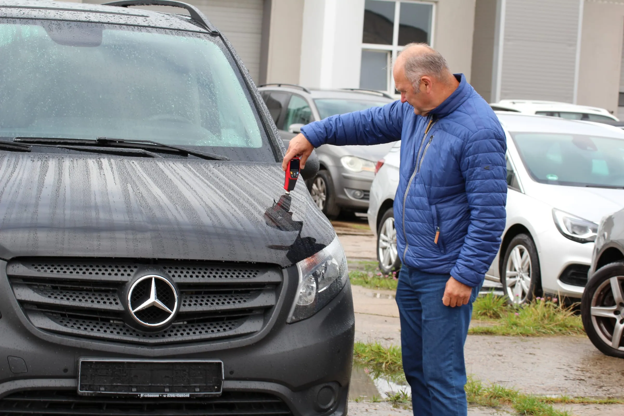Ekspertas su dažų storio matuokliu tikrina automobilį prekybos aikštelėje